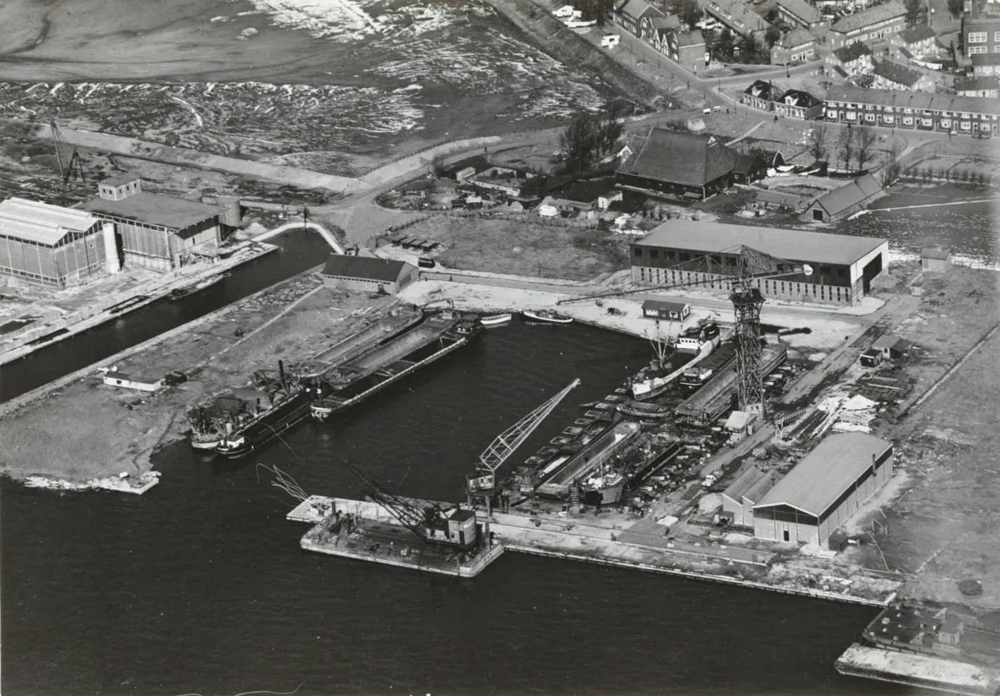 Luchtfoto uit 1955: de pas gegraven insteekhaven met binnenvaartschepen, kranen en loodsen, met rechtsboven de dijkhuizen van Nieuwendam. Linksboven wijst een pijl het pand met de kraan aan dat het latere Gembo-gebouw wordt.