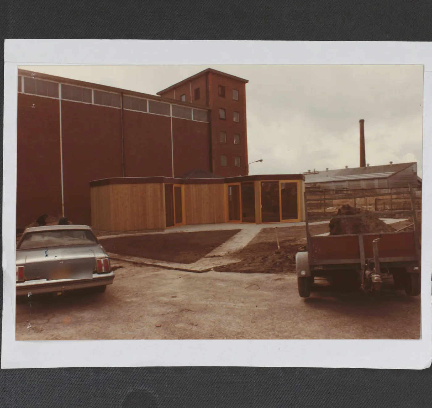 Kleurenfoto uit maart 1985: de bakstenen fabriekstoren met schoorsteen en een houten uitbouw in aanbouw.