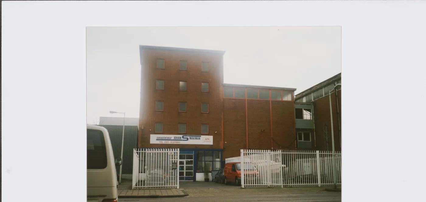 Kleurenfoto van de westgevel in 2002, met het bord van Garagebedrijf Johan Smakman aan de gevel.