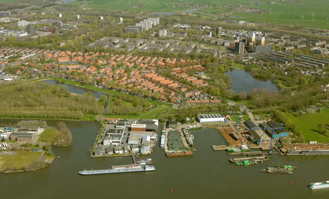 Luchtfoto uit 2015: het Gembo-terrein als schiereiland in het IJ, met daarachter het groen en de rode daken van tuindorp Nieuwendam.